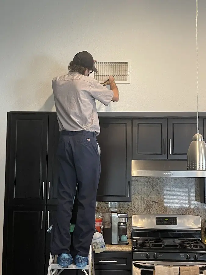 Technician inspecting an air vent during HVAC service in Henniker